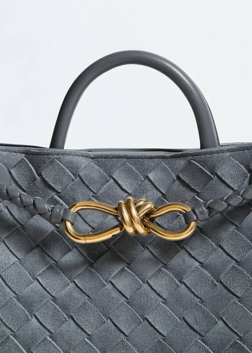 Gray woven handbag with a gold bow detail on a light gray background
