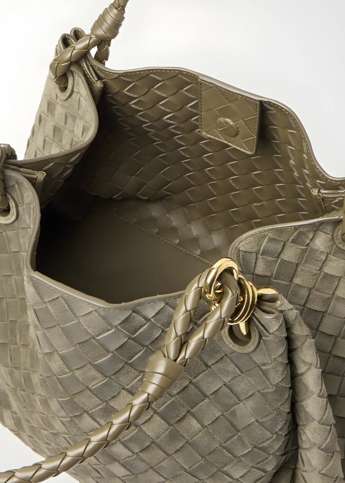 Close-up of a woven handbag with braided handle and gold accent on a white background