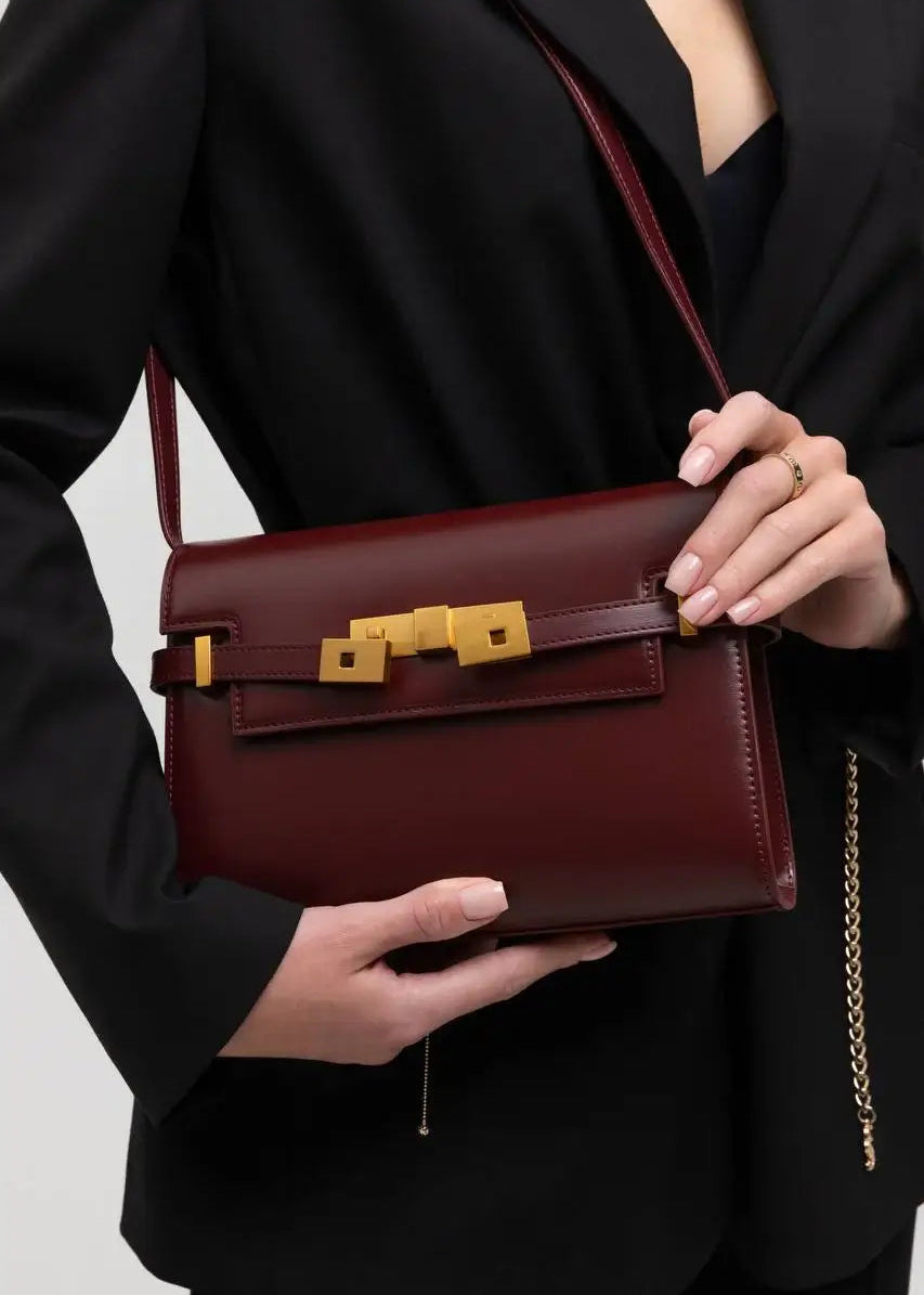 Person holding a maroon handbag with gold accents against a neutral background