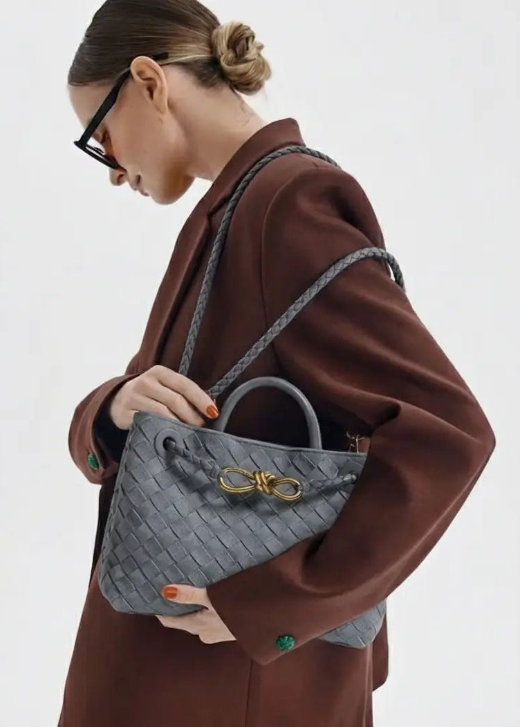 Person wearing a brown coat holding a gray handbag with a gold clasp on a white background