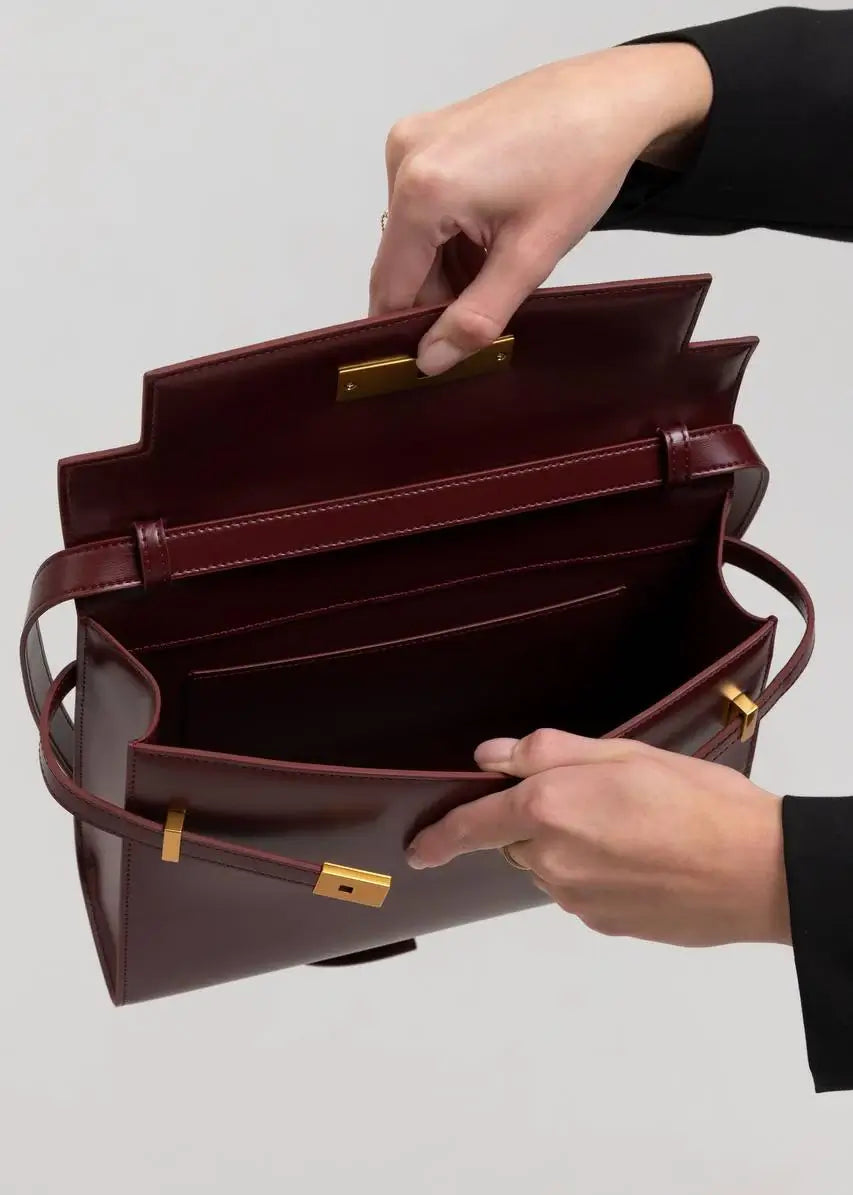 Brown leather briefcase with gold hardware held open by a hand on a light gray background