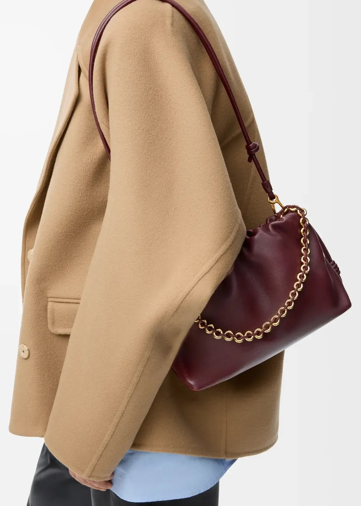 Person wearing a beige coat holding a burgundy handbag with gold chain detail on a light gray background