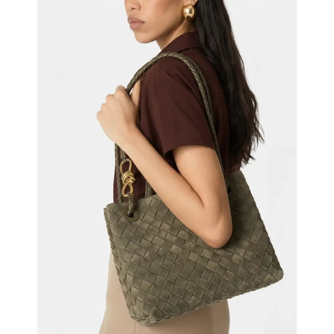 Woman holding a woven green handbag against a plain background
