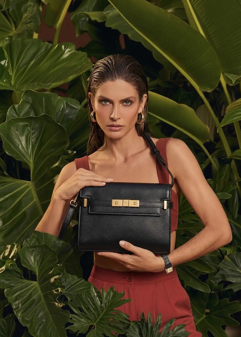Woman holding a black handbag with 'COC' branding in front of green foliage