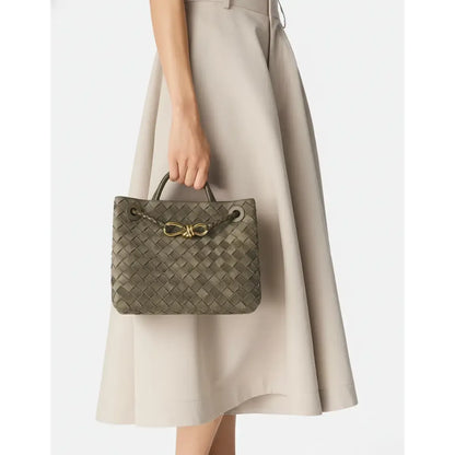 Person holding a woven handbag with a gold bow detail against a neutral background