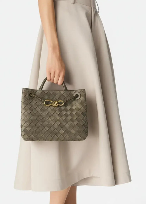 Person holding a woven handbag with a gold bow detail against a neutral background