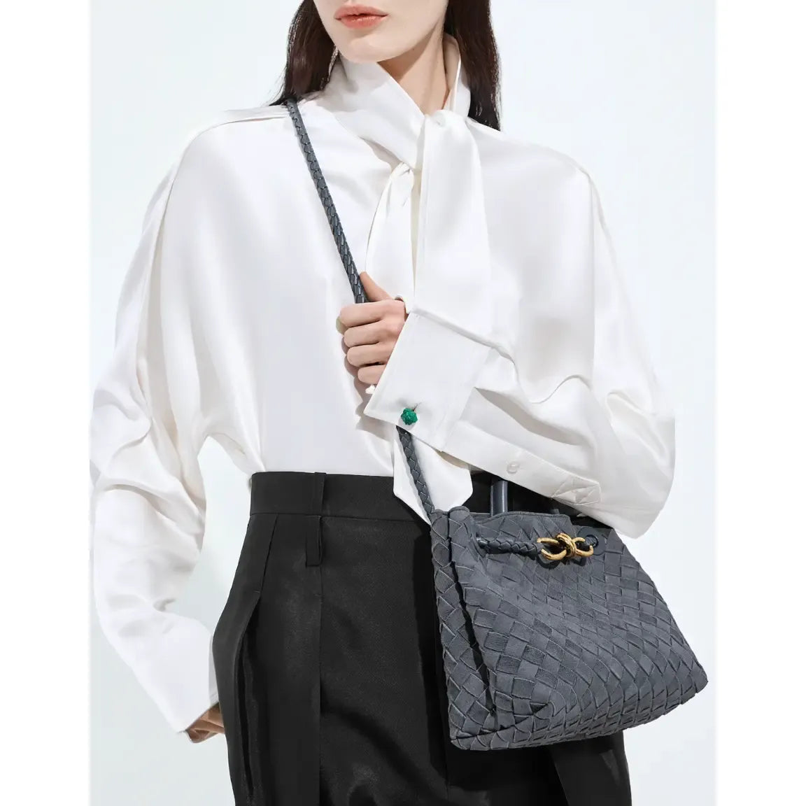 Person holding a gray textured handbag with a white shirt and black pants on a light background