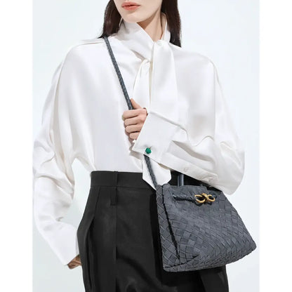 Person holding a gray textured handbag with a white shirt and black pants on a light background