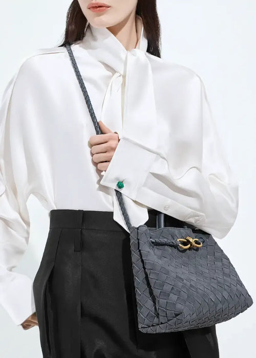 Person holding a gray textured handbag with a white shirt and black pants on a light background
