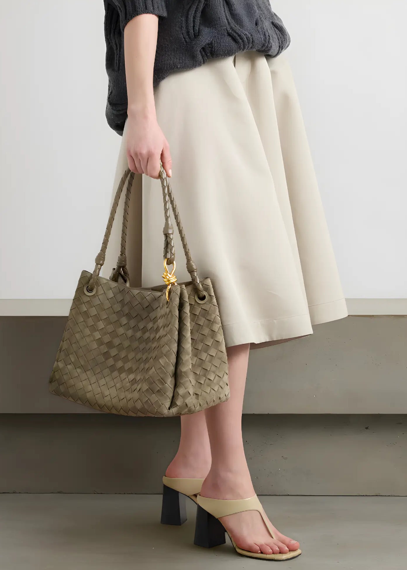 Person holding a woven handbag with a plain background