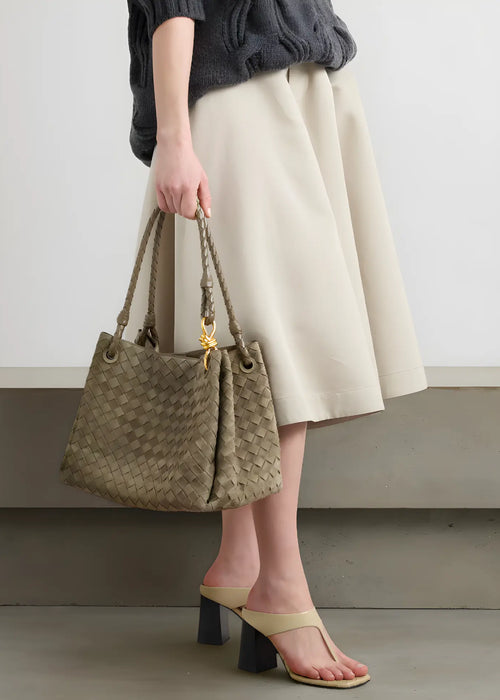 Person holding a woven handbag with a plain background