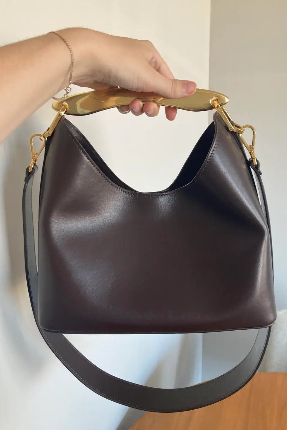 Brown leather handbag with gold accents held by a hand against a neutral background