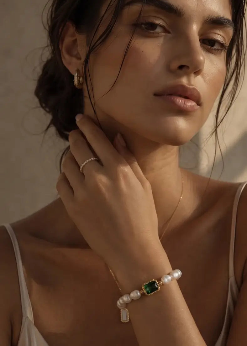 A close-up lifestyle shot of a woman wearing a beaded bracelet with white pearls and a green rectangular stone, along with matching pearl and gold jewelry.