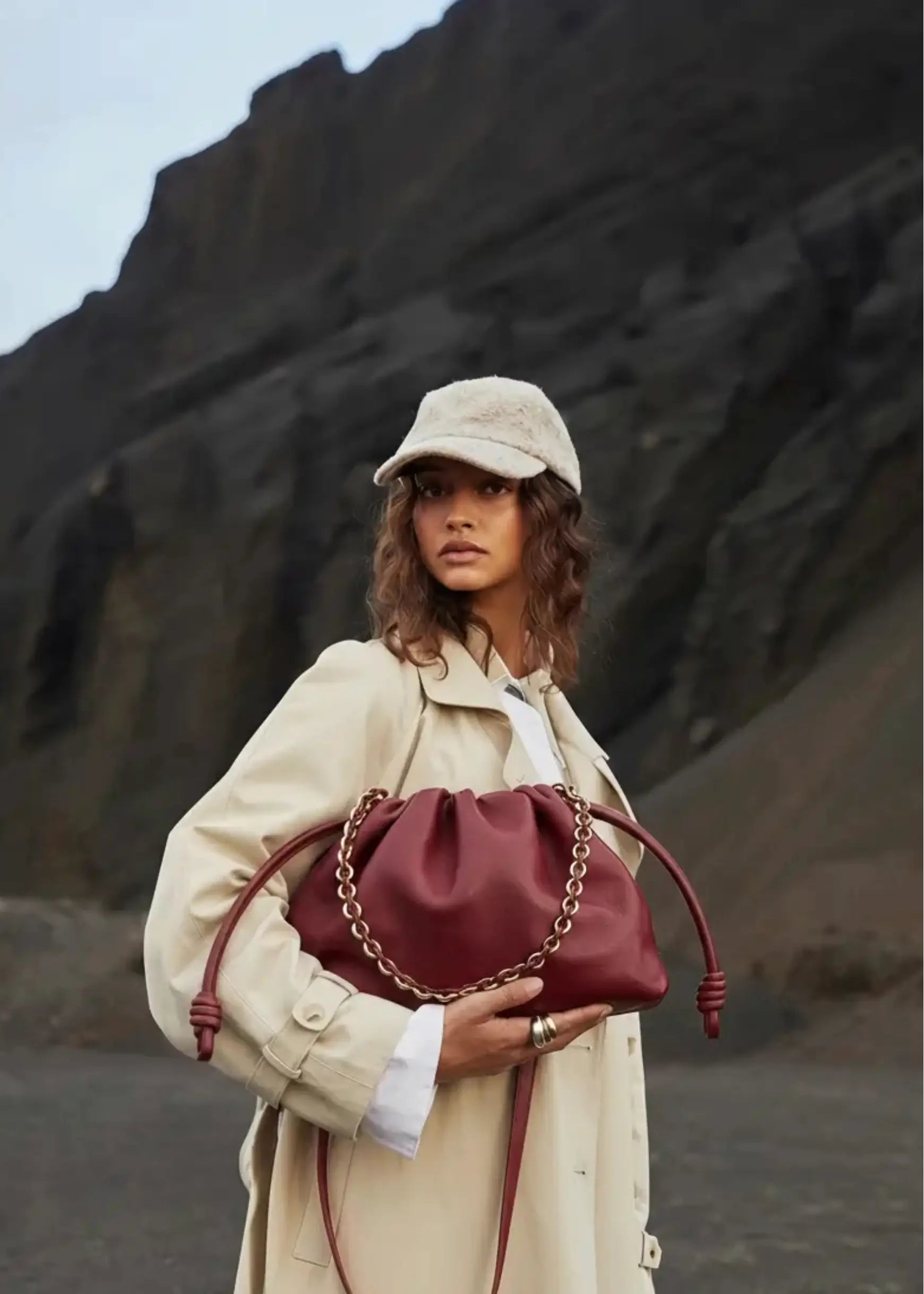 Person holding a maroon handbag against a rocky background
